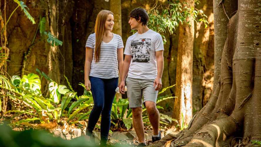 A photo of a woman and man standing in a forest holding hands