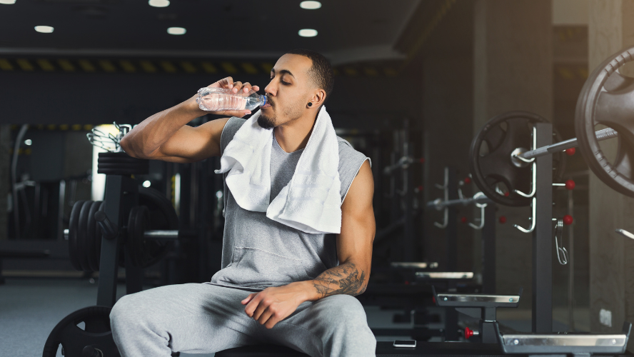 A man sits in a gym drinking a bottle of water