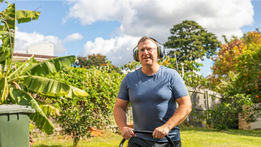 A man wearing ear protection mowing the lawn